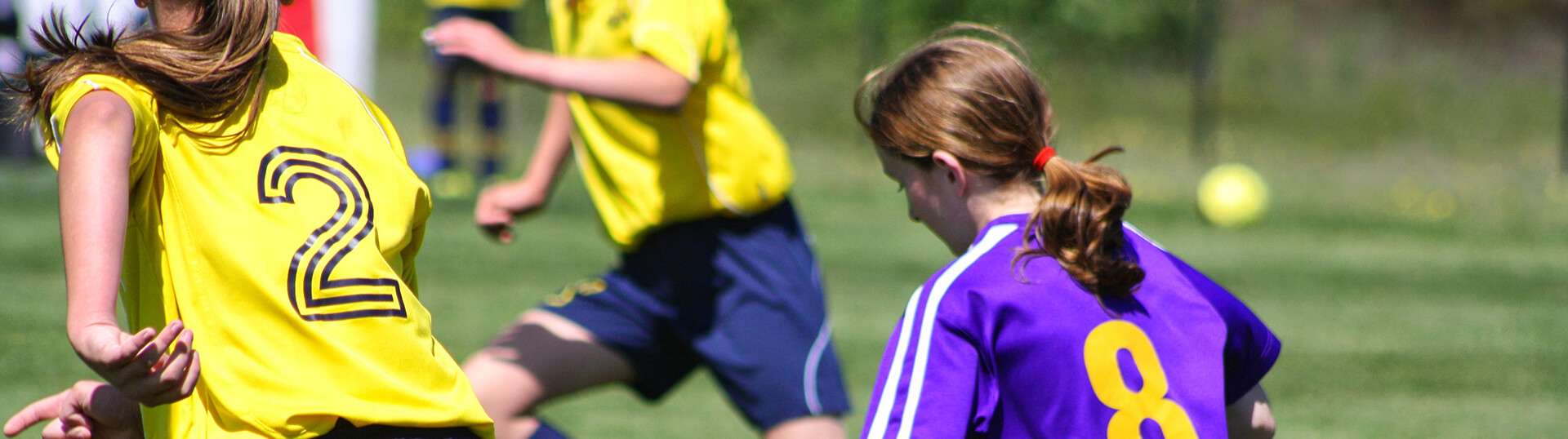 A group of soccer players chase the ball, facing away from the camera